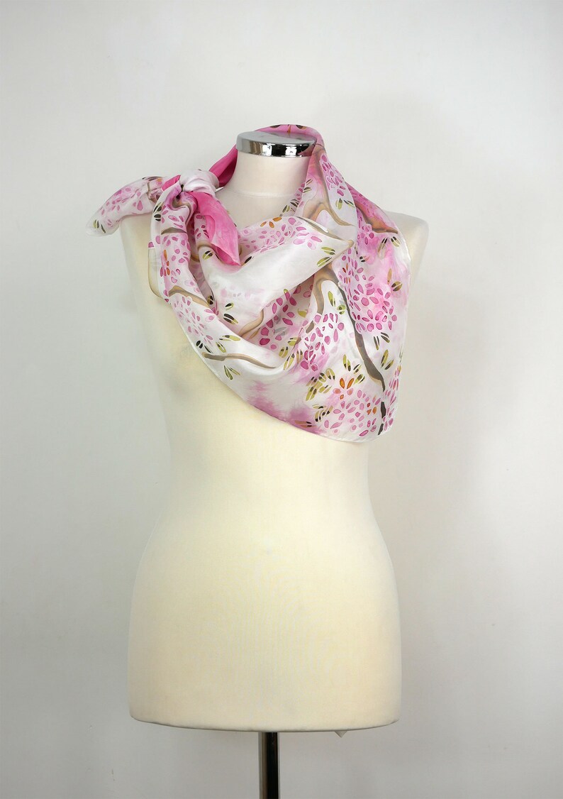 May include: A white silk scarf with a pink floral pattern. The scarf is tied around a white mannequin's neck.