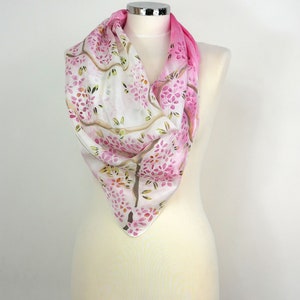 May include: A white silk scarf with a pink ombre design and a floral pattern. The scarf is draped over a white mannequin.