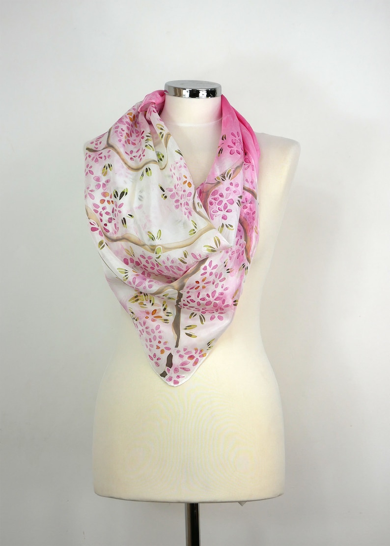 May include: A white silk scarf with a pink ombre design and a floral pattern. The scarf is draped over a white mannequin.