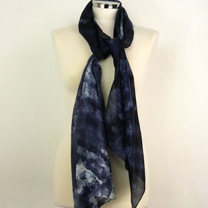 Op de afbeelding: Een donkerblauwe zijden sjaal met een wit en grijs tie-dye patroon. De sjaal is gedrapeerd over een wit mannequin.