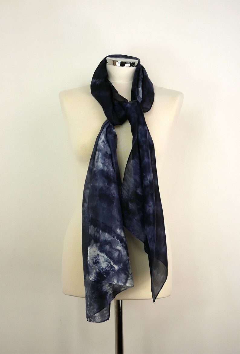 Op de afbeelding: Een donkerblauwe zijden sjaal met een wit en grijs tie-dye patroon. De sjaal is gedrapeerd over een wit mannequin.