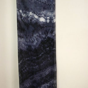 Op de afbeelding: Een lange, rechthoekige sjaal met een tie-dye patroon in tinten blauw en wit. De sjaal hangt aan een waslijn.