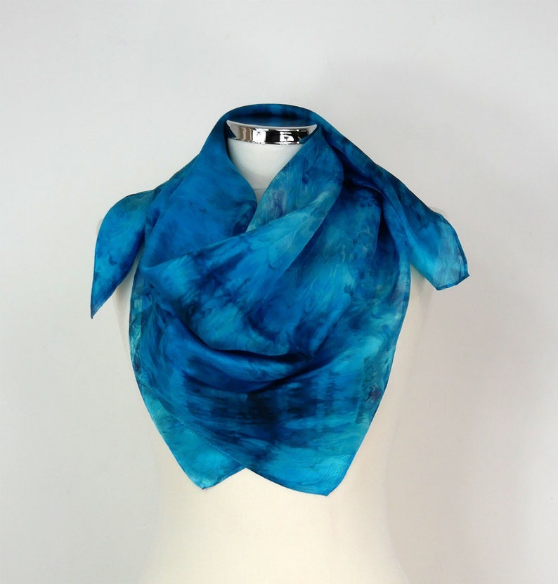 May include: A blue silk scarf with a tie-dye pattern. The scarf is folded and displayed on a mannequin.