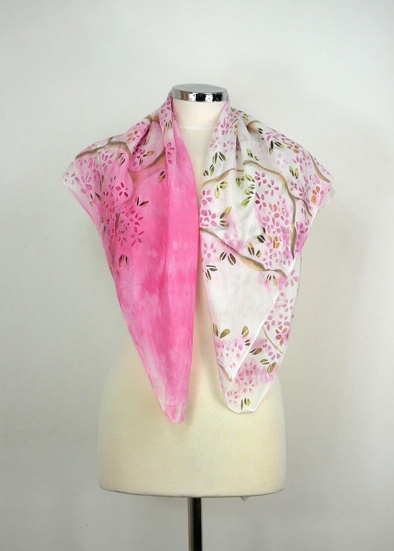May include: A pink and white silk scarf with a floral pattern. The scarf is folded and displayed on a white mannequin.