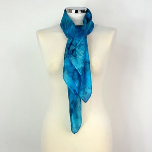 May include: A blue silk scarf with a tie-dye pattern. The scarf is displayed on a white mannequin.