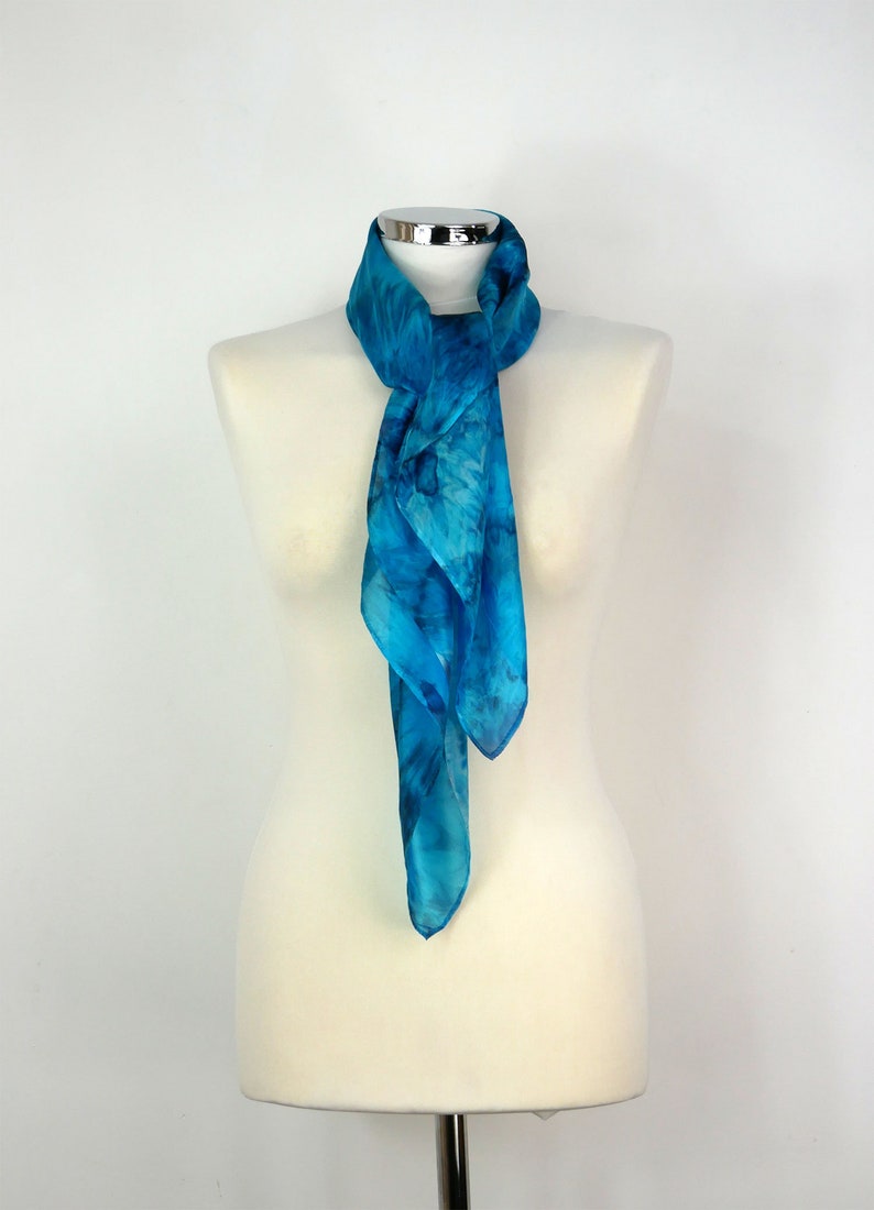 May include: A blue silk scarf with a tie-dye pattern. The scarf is displayed on a white mannequin.
