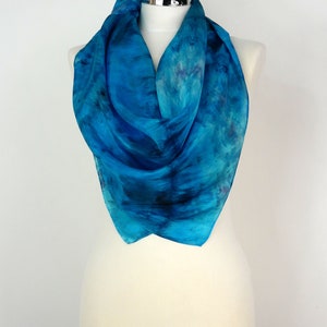 May include: A blue silk scarf with a tie-dye pattern. The scarf is draped over a white mannequin.