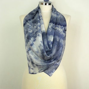 May include: A blue and white silk scarf with a tie-dye pattern. The scarf is draped over a white mannequin.