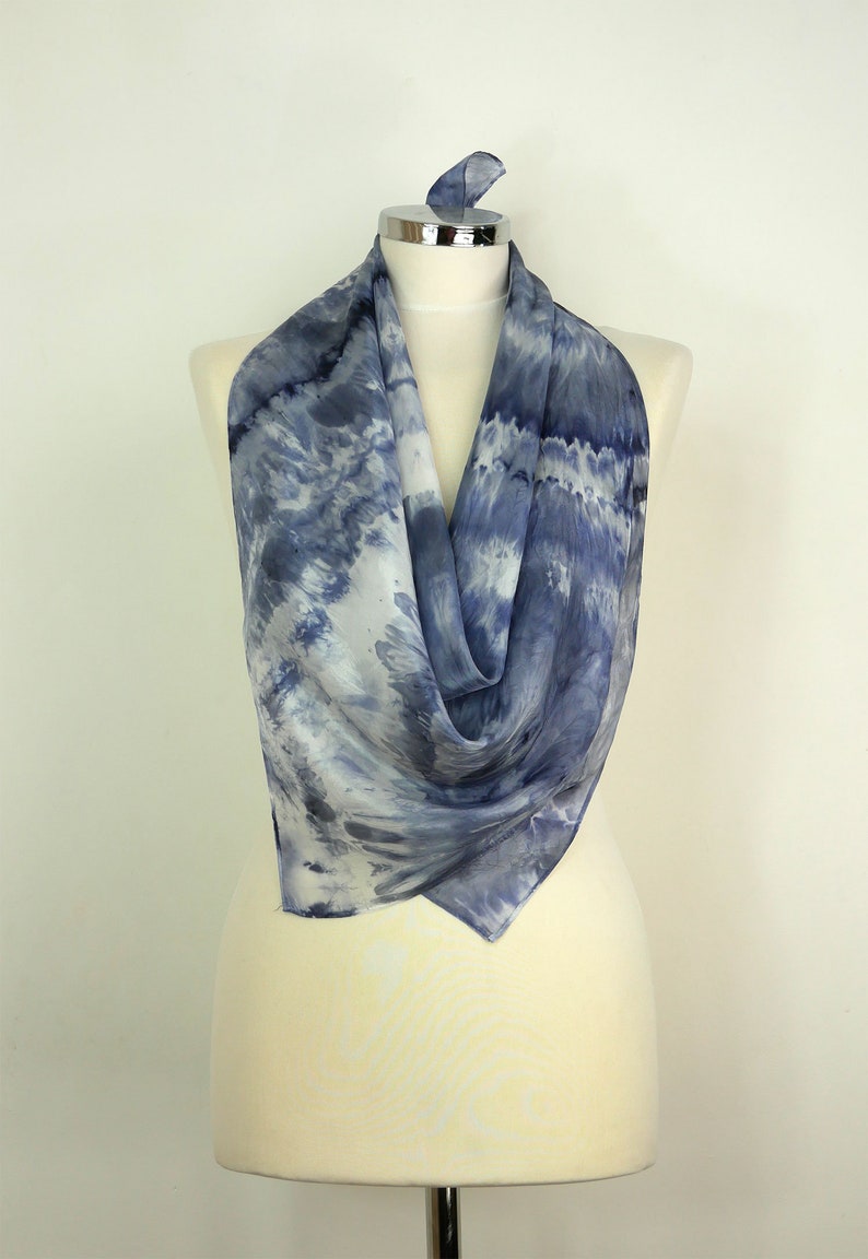 May include: A blue and white silk scarf with a tie-dye pattern. The scarf is draped over a white mannequin.