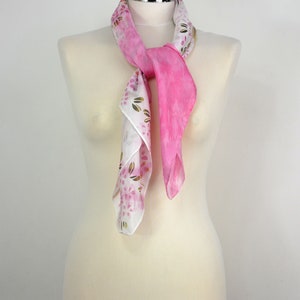 May include: A pink and white silk scarf with a floral pattern. The scarf is tied around a white mannequin's neck.