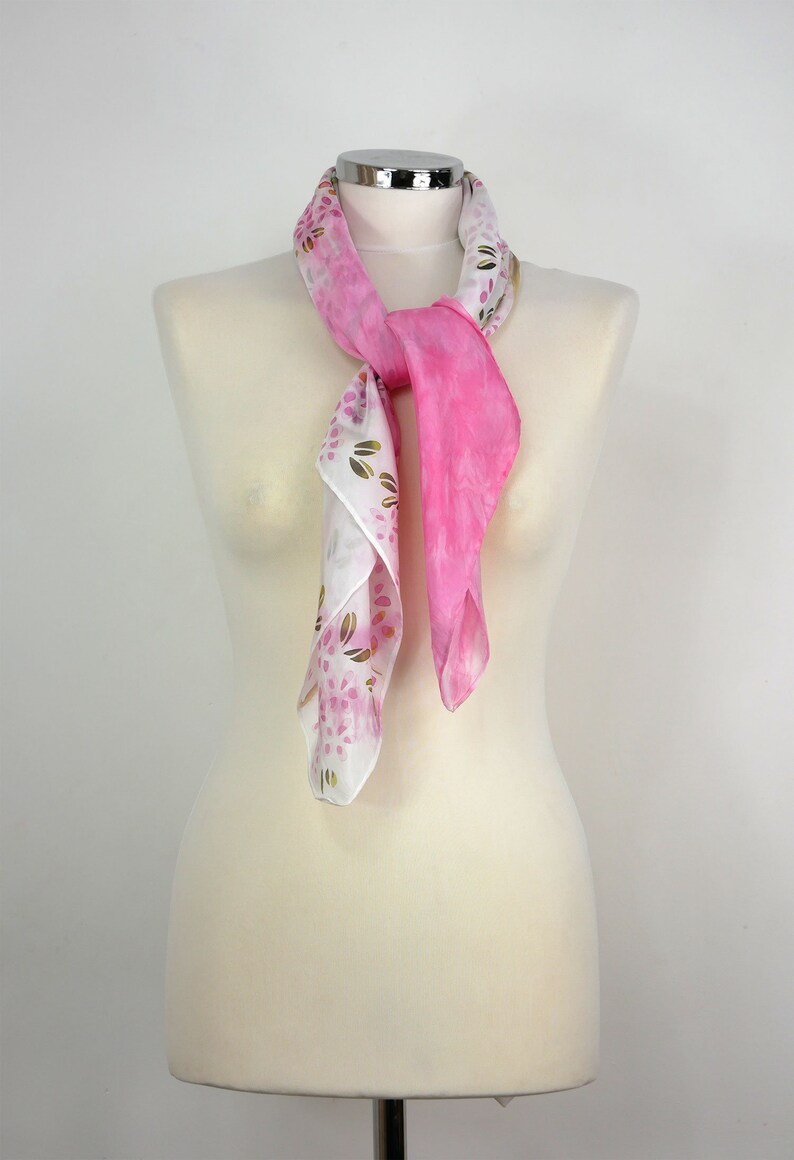 May include: A pink and white silk scarf with a floral pattern. The scarf is tied around a white mannequin's neck.