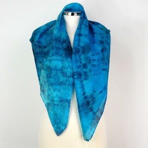 May include: A blue silk scarf with a tie-dye pattern. The scarf is displayed on a white mannequin.