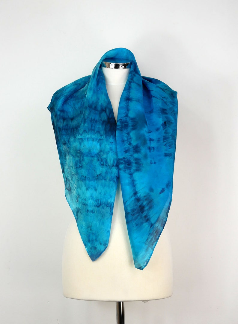 May include: A blue silk scarf with a tie-dye pattern. The scarf is displayed on a white mannequin.