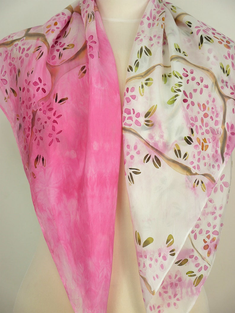 May include: A pink and white silk scarf with a floral pattern. The scarf is hand-painted with a design of branches and flowers.