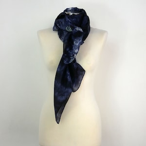 Op de afbeelding: Een blauwe zijden sjaal met een tie-dye patroon. De sjaal is gedrapeerd om een wit mannequin.