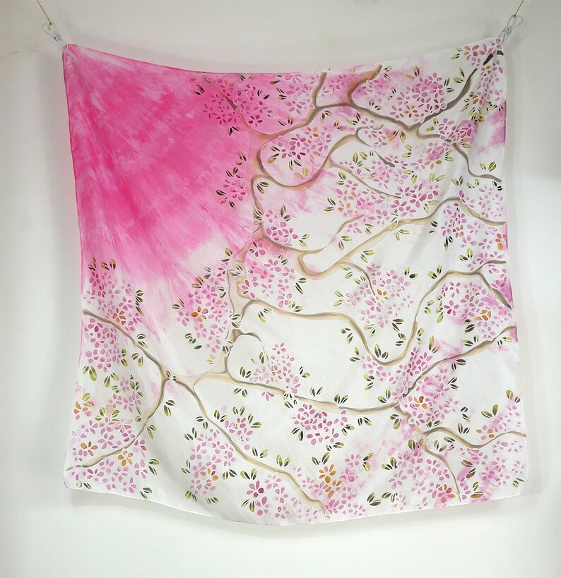 May include: A white silk scarf with a pink and green floral design. The design features a tree with branches and leaves, and pink flowers.