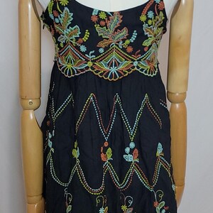 May include: Black spaghetti strap dress with colourful floral embroidery. The dress features intricate embroidery in shades of orange, green, yellow, and blue. The dress is displayed on a mannequin.