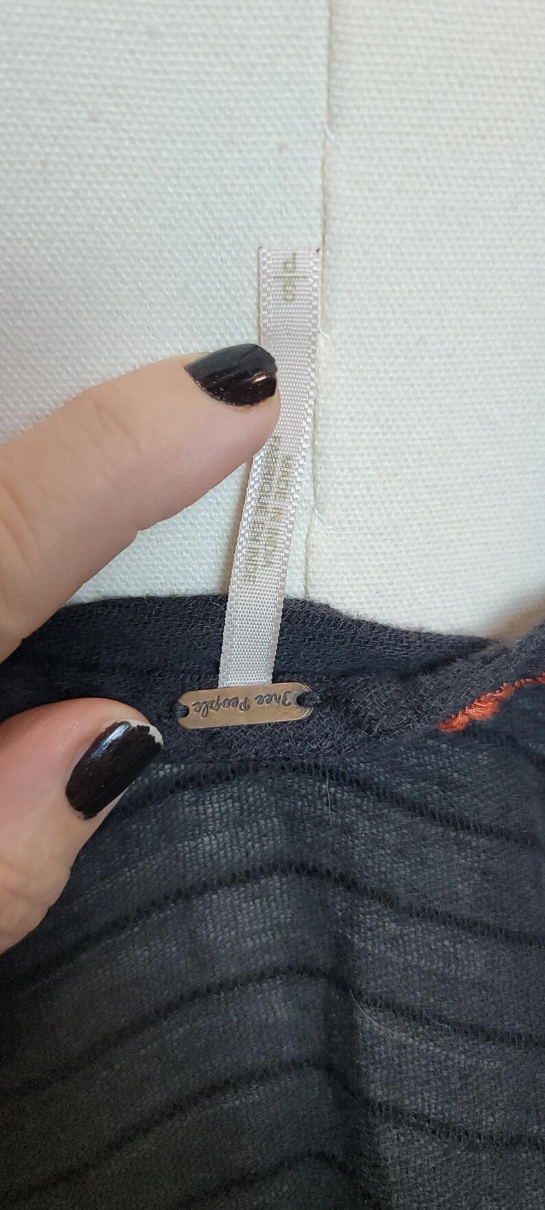 Puede incluir: Primer plano de una camiseta gris oscuro con rayas horizontales y un acento naranja. La etiqueta dice "Free People". La camiseta est&aacute; sobre un maniqu&iacute; blanco.