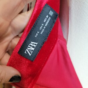 May include: Close-up of a red velvet garment with a black label. The label reads "ZARA" and includes size and origin information: EUR S, USA S, MEX 26, Made in Morocco.