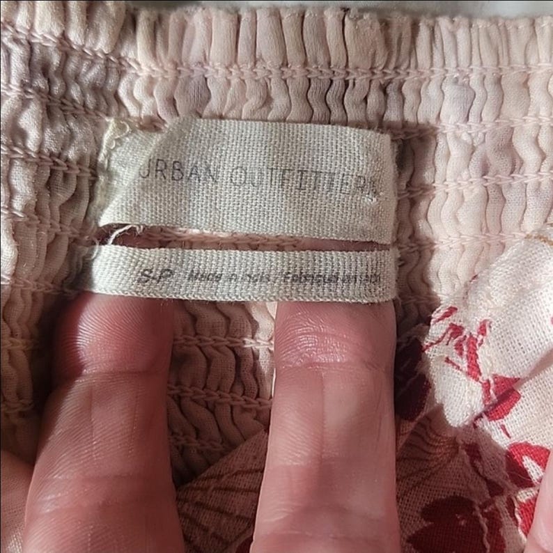Puede incluir: Primer plano de una tela rosa claro y blanca con un estampado floral. La tela est&aacute; fruncida con el&aacute;stico. Una etiqueta dice "URBAN OUTFITTERS" y "S/P Made in India / Fabriqu&eacute; en Inde."