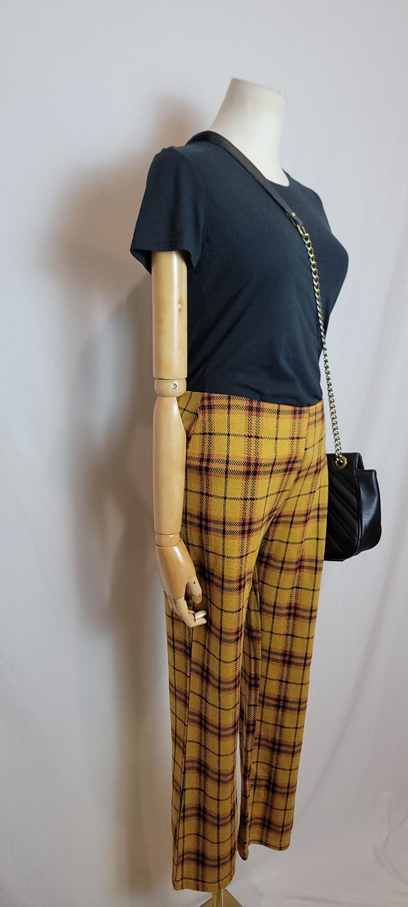K&ouml;nnte beinhalten: Eine Schaufensterpuppe zeigt ein schwarzes T-Shirt und eine gelbe karierte Hose mit einer schwarzen Handtasche. Die Hose hat eine senfgelbe Basis mit einem rot-schwarzen Karomuster. Die Handtasche hat einen Kettenriemen.