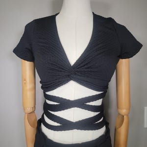 May include: Black crop top with a twisted front and criss-cross straps at the waist.