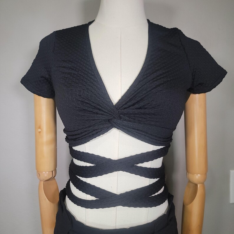 May include: Black crop top with a twisted front and criss-cross straps at the waist.
