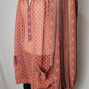 Puede incluir: Blusa color coral con estampado floral y rayas verticales marrones. La blusa tiene cuello en V, detalles de botones y bolsillos. El escote y las mangas est&aacute;n adornados con adornos azules y coloridos.