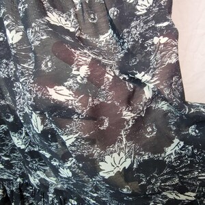 Puede incluir: Primer plano de una tela negra transparente con un estampado floral blanco. La tela es ligera y parece ser un material de vestido o blusa. El dise&ntilde;o incluye flores y follaje estilizados, creando una est&eacute;tica delicada y aireada.