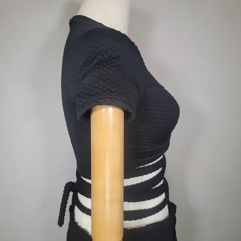 May include: Black crop top with short sleeves and a criss-cross design at the waist.