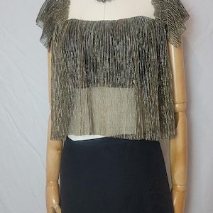 May include: A gold and black metallic crop top with a square neckline and short sleeves is displayed on a mannequin. The top is paired with a black mini skirt. A multi-strand beaded necklace is also included.