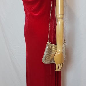 May include: A red velvet gown with a cowl neckline and a small, silver mesh purse with a chain strap. The dress is displayed on a mannequin. The purse is approximately 6 inches wide and 4 inches tall.