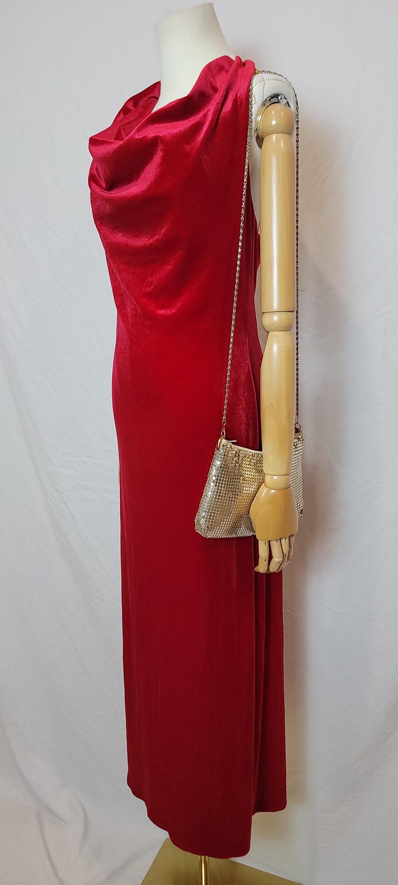 May include: A red velvet gown with a cowl neckline and a small, silver mesh purse with a chain strap. The dress is displayed on a mannequin. The purse is approximately 6 inches wide and 4 inches tall.