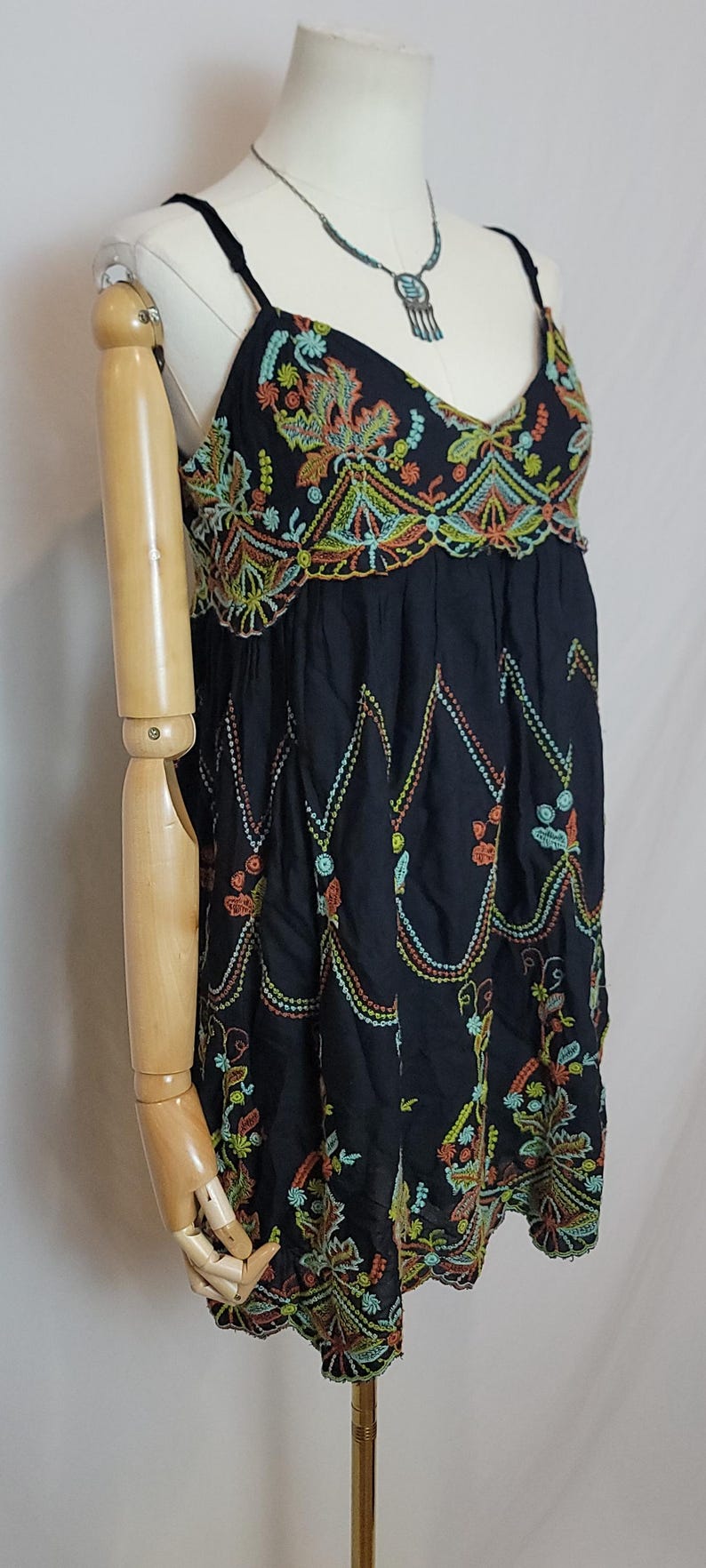 May include: Black embroidered tank top with colourful floral and geometric patterns. The top has a V-neck and thin straps. The embroidery includes orange, green, and yellow details. The garment is displayed on a mannequin.