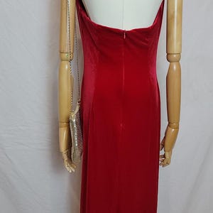 May include: A red velvet gown with a halter neckline and a back zipper. The dress has a floor-length skirt with a slit. A silver mesh purse hangs from the mannequin's arm.