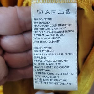 May include: A white clothing tag with black text, featuring washing instructions. The tag lists fabric composition as 90% polyester and 10% spandex. Instructions include hand washing in cold water, no wringing, and low-temperature ironing.