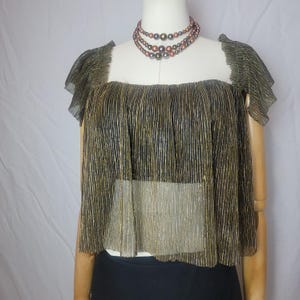 May include: A gold and black pleated top with short sleeves is displayed on a mannequin. The top has a square neckline and a layered design. A multi-strand beaded necklace in shades of brown and bronze is also visible.