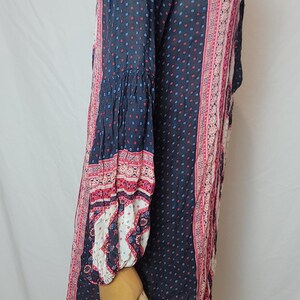 May include: A long-sleeved navy blue dress with a small square pattern in red and blue. The dress features pink and white patterned panels down the sides and on the sleeves. The sleeves have a bell shape at the wrist.
