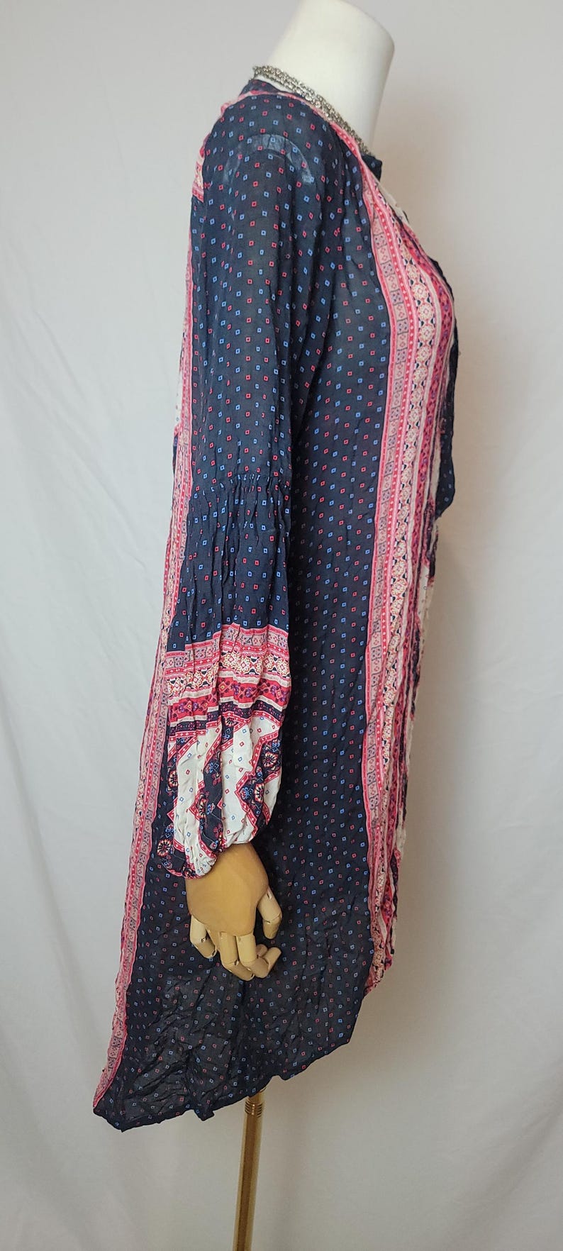 May include: A long-sleeved navy blue dress with a small square pattern in red and blue. The dress features pink and white patterned panels down the sides and on the sleeves. The sleeves have a bell shape at the wrist.