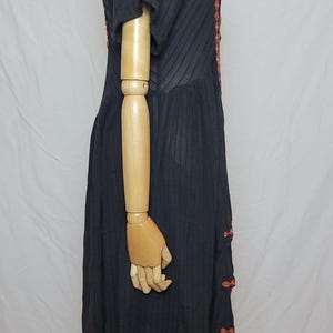 Puede incluir: Vestido negro de manga corta con textura acanalada vertical. El vestido presenta bordados naranjas a lo largo del escote y en el lateral. El vestido se exhibe en un maniqu&iacute;.