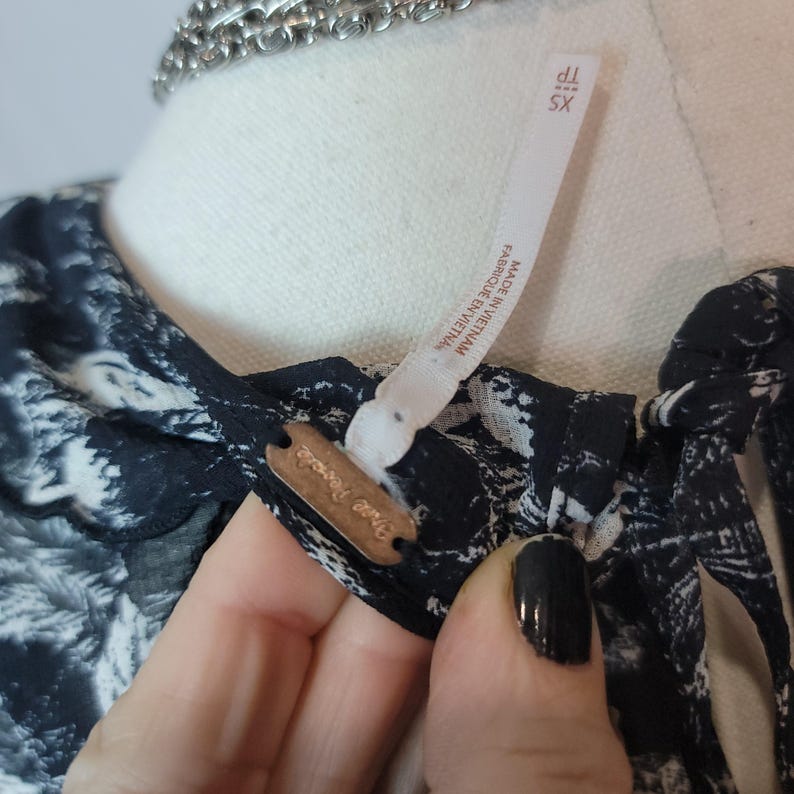 Puede incluir: Primer plano de un top con estampado en blanco y negro con una etiqueta que dice "Free People" y "XS". El top est&aacute; hecho en Vietnam. Una cadena de plata es visible en el fondo.