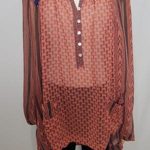 Puede incluir: T&uacute;nica color coral con estampado floral y mangas largas. La parte superior presenta una botonadura frontal, dos bolsillos y adornos decorativos a lo largo del escote. Las mangas y los laterales tienen un dise&ntilde;o a rayas. La t&uacute;nica se exhibe en un maniqu&iacute;.