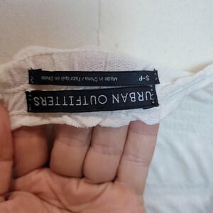 Op de afbeelding: Close-up van een wit kledinglabel met de tekst "URBAN OUTFITTERS" in wit op een zwarte achtergrond. Onder het label staat een ander label met de tekst "Made in China / Fabriqu&eacute; en Chine" en "S-P".