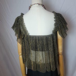 May include: A gold and black pleated top with a square neckline and ruffled sleeves is displayed on a mannequin. The sheer fabric has vertical gold stripes. A beaded necklace is around the mannequin's neck. The top is paired with a black garment.