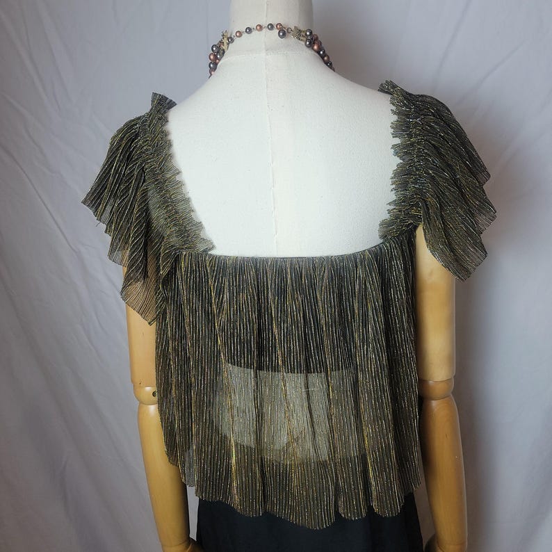 May include: A gold and black pleated top with a square neckline and ruffled sleeves is displayed on a mannequin. The sheer fabric has vertical gold stripes. A beaded necklace is around the mannequin's neck. The top is paired with a black garment.