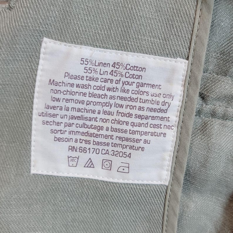 May include: A close-up of a white care label sewn into a light green garment. The label provides washing instructions in English and French, detailing washing, bleaching, drying, and ironing. The fabric is 55% linen and 45% cotton.