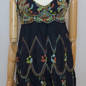 May include: Black spaghetti strap dress with colourful embroidered floral and geometric patterns. The dress features a V-neckline and a fitted bodice, displayed on a mannequin. A silver necklace with a pendant is also visible.