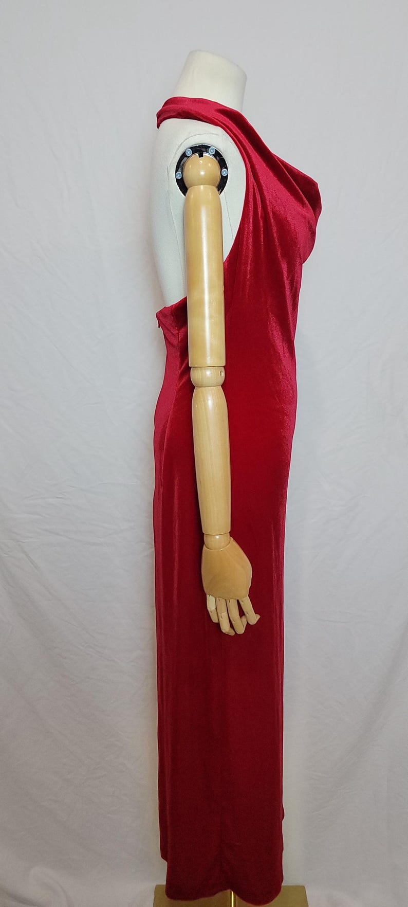 May include: A vibrant red, floor-length dress with a draped cowl neckline. The dress is sleeveless and has a fitted silhouette, showcasing a sleek and elegant design. The dress is displayed on a mannequin.