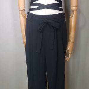 May include: A black crop top with a twist detail and a tie front. The top is paired with black wide-leg trousers with a high waist and a tie belt.