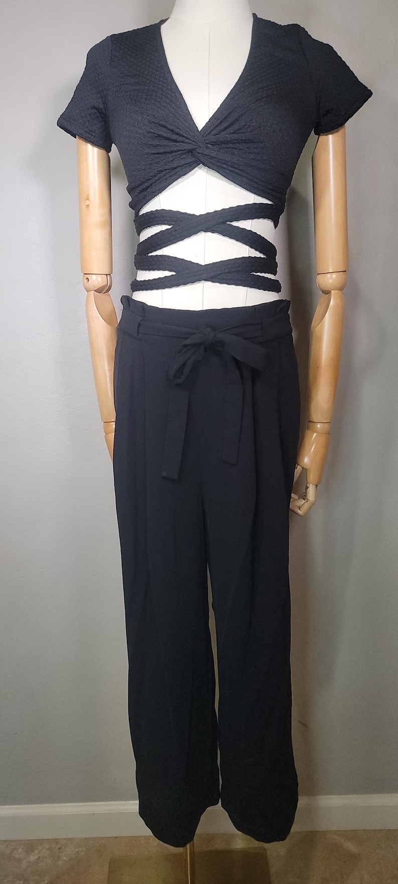 May include: A black crop top with a twist detail and a tie front. The top is paired with black wide-leg trousers with a high waist and a tie belt.